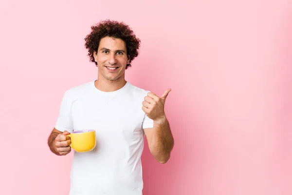 Joven Hombre Rizado Caucásico Sosteniendo Una Taza Sonriendo Levantando Pulgar — Foto de Stock