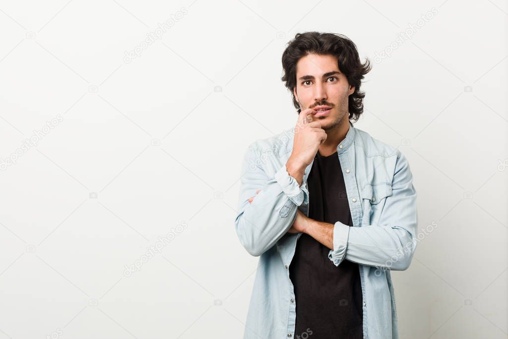 Young handsome man against a white background relaxed thinking about something looking at a copy space.