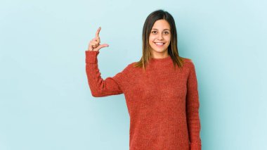 Mavi arka planda izole edilmiş genç bir kadın işaret parmaklarıyla küçük bir şey tutuyor, gülümsüyor ve kendinden emin..