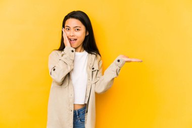 Sarı arka planda izole edilmiş genç Çinli kadın avuç içinde fotokopi alanı tutuyor, el üstünde tutuyor. Şaşırmış ve mutlu..