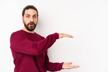 Uzun saçlı genç adam beyaz bir arka planda izole edilmiş. Ellerinin arasında bir kopya alanı tutarken şok olmuş ve hayrete düşmüş..