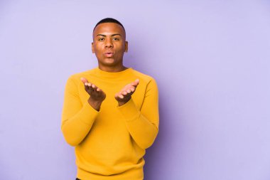 Mor arka planda izole edilmiş genç latin adam dudakları katlıyor ve hava öpücüğü göndermek için avuç içleri tutuyor..