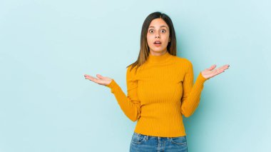 Mavi arka planda izole genç bir kadın şaşırmış ve şok olmuş..