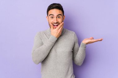 Mor arka planda izole edilmiş genç beyaz bir adam avuç içinde fotokopi alanı tutuyor, el üstünde tutuyor. Şaşırmış ve mutlu..