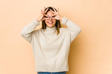 Bej arka planda izole edilmiş genç bir kadın gözlerde sorun olmadığını gösteriyor.