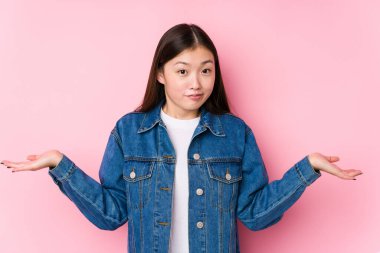 Pembe arka planda poz veren Çinli genç bir kadın şüpheli davranıp omuz silkiyor..