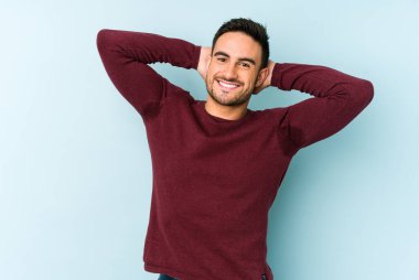 Mavi arka planda izole edilmiş genç beyaz adam kollarını uzatıyor, rahat bir konumda..