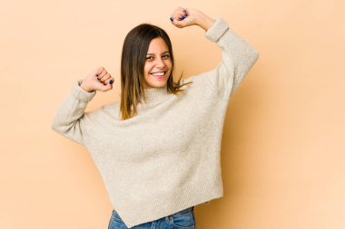 Bej arka planda izole edilmiş genç bir kadın özel bir günü kutluyor, atlıyor ve enerji ile kollarını kaldırıyor..