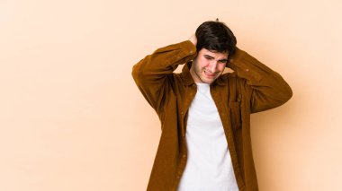 Bej arka planda izole edilmiş genç bir adam kulakları elleriyle kapatıyor..