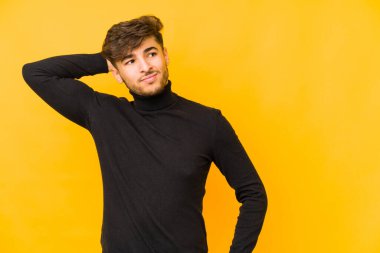 Sarı arka planda izole edilmiş genç bir Arap adam kafasının arkasına dokunuyor, düşünüyor ve bir seçim yapıyor..