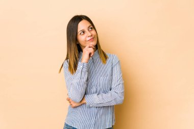 Bej arka planda izole edilmiş genç bir kadın şüpheli ve şüpheci bir ifadeyle yana bakıyor..