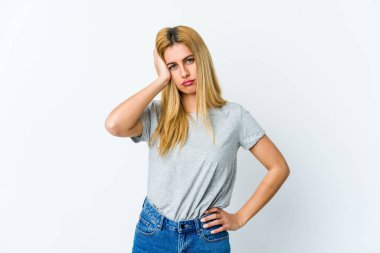 Beyaz arka planda izole edilmiş genç sarışın kadın yorgun ve uykulu. Elini başının üstünde tutuyor..
