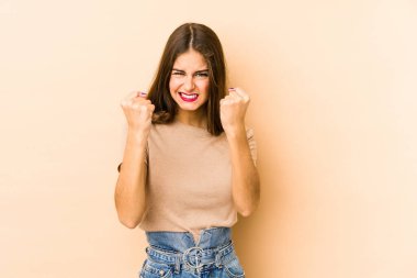 Beyazlı genç bir kadın bej arka planda izole edilmiş. Kameraya yumruk, agresif yüz ifadesi gösteriyor..