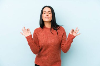 Mavi arka planda izole edilmiş genç beyaz kadın yoğun bir günün ardından rahatlıyor, yoga yapıyor..