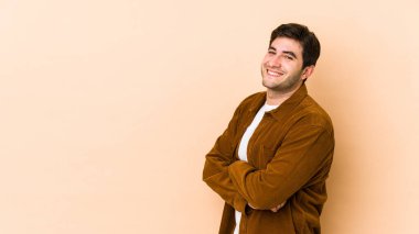 Bej arka planda izole genç bir adam kendinden emin, kararlılıkla kollarını kavuşturuyor..