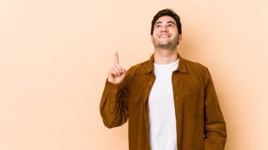 Bej arka planda izole genç adam iki ön parmağı da boş bir alan gösteriyor.