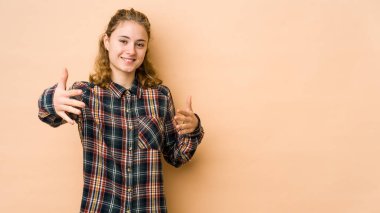 Beyazlı genç bir kadın bej arka planda izole edilmiş kameraya sarılıyor..