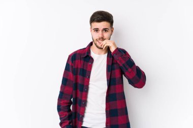 Beyaz arka planda poz veren genç beyaz bir adam tırnak yiyor, gergin ve endişeli..