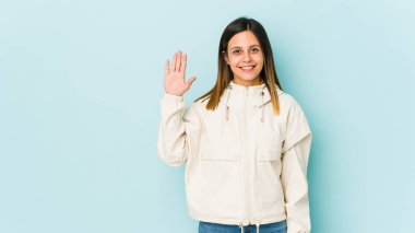 Mavi arka planda izole edilmiş genç bir kadın gülümseyerek beş numarayı parmaklarıyla gösteriyor..