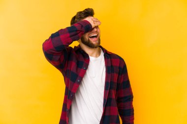 Sarı arka planda izole edilmiş genç beyaz adam elleriyle gözlerini kapatıyor, geniş bir gülümsemeyle bir sürpriz bekliyor..