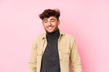 Arka planda poz veren genç bir Arap, yalnız gülüyor, gözlerini kapıyor, rahat ve mutlu hissediyor..