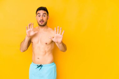 Sarı arka planda mayosu olan genç beyaz bir adam yakın bir tehlike nedeniyle şoka uğrayan genç beyaz bir adam.