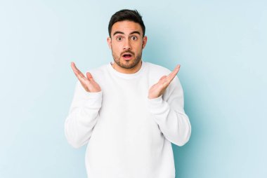 Kafkasyalı genç adam mavi arka planda izole edildi. Şaşırdı ve şok oldu..