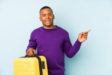 Genç bir gezgin, izole edilmiş bir bavul tutuyor gülümsüyor ve boş bir alanda bir şey gösteriyor..