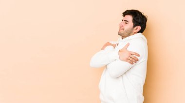 Genç adam bej rengi arka plan kucaklamalarında yalnız, kaygısız ve mutlu gülümsüyor..