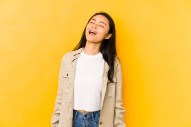 Sarı arka planda izole edilmiş genç Çinli kadın gevşemiş ve mutlu bir şekilde gülüyor, boynunu uzatmış dişlerini gösteriyor..