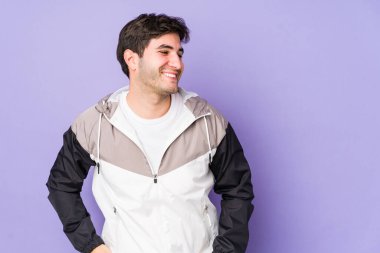 Mor arka planda izole edilmiş genç adam mutlu bir şekilde gülüyor ve ellerini karnının üstünde tutarak eğleniyor..