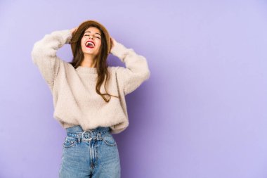 Mor arka planda soyutlanmış beyaz bir kadın ellerini başının üstünde tutarak neşe içinde gülüyor. Mutluluk kavramı.