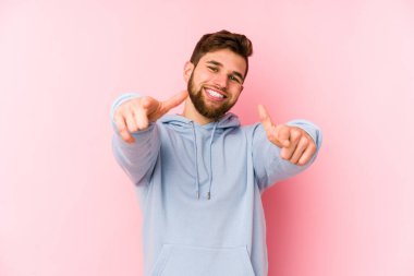 Pembe arka planda izole edilmiş genç beyaz adam. Önü işaret eden neşeli gülümsemeler..