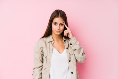 Pembe arka planda poz veren beyaz bir kadın şakağı parmağıyla işaret ediyor, düşünüyor ve bir göreve odaklanıyor..