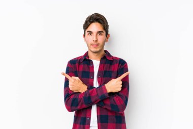 Pembe arka planda yalnız bırakılmış noktalarda poz veren genç beyaz adam iki seçenek arasında seçim yapmaya çalışıyor..