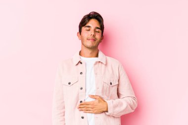 Pembe arka planda poz veren beyaz bir genç göbeğe dokunuyor, nazikçe gülümsüyor, yemek yiyor ve tatmin oluyor..