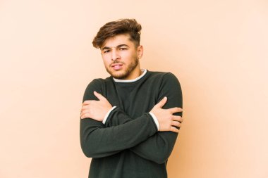 Bej bir arka planda izole genç bir Arap adam düşük sıcaklık veya hastalık nedeniyle soğuyor.