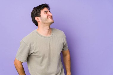 Mor arka planda izole olmuş genç adam gevşemiş ve mutlu bir şekilde gülüyor, boynunda dişler var..