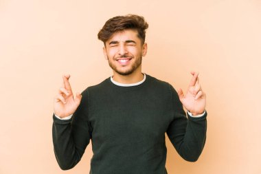 Genç Arap bir adam bej arka planda izole edilmiş şans dilemek için şans diliyor.