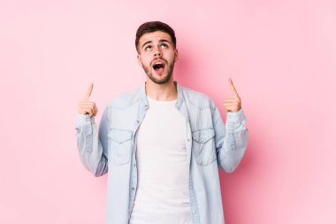 Beyaz arka planda poz veren beyaz tenli genç bir iş adamı ağzı açık bir şekilde üst tarafı işaret ediyor..