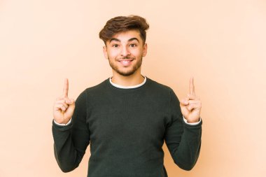 Bej bir arka planda izole genç bir Arap adam işaret iki ön parmakları boş bir boşluk gösteren.