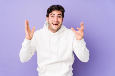 Mor arka planda izole genç bir adam hoş bir sürpriz alıyor, heyecanlı ve el kaldırıyor..