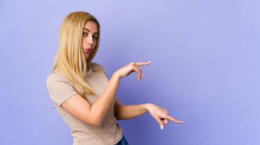 Mor arka planda izole edilmiş genç sarışın kadın işaret parmaklarıyla fotokopi alanını işaret ederek heyecan ve arzuyu ifade ediyor..