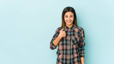 Mavi arka planda izole edilmiş genç bir kadın parmağını göstererek şaşırdı, geniş bir gülümsemeyle..