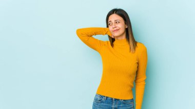 Mavi arka planda izole edilmiş genç bir kadın kafasının arkasına dokunuyor, düşünüyor ve bir seçim yapıyor..