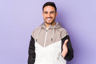 Mor arka planda izole edilmiş genç beyaz adam selamlama jesti olarak kameraya elini uzatıyor..