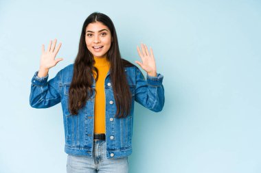 Genç Hintli kadın mavi arka planda izole edilmiş. Hoş bir sürpriz bekliyor. Heyecanlı ve el kaldırıyor..