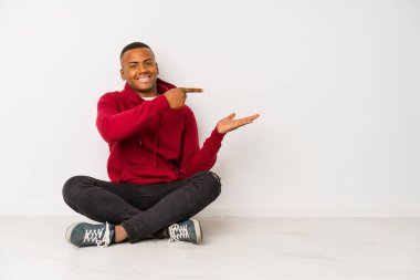 Yerde oturan genç latin adam heyecanlı bir şekilde avucunun içinde bir kopya tutuyor..