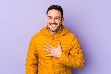 Mor arka planda izole olmuş genç beyaz adam yüksek sesle gülüyor elini göğsüne koyuyor..