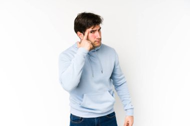 Beyaz arka planda izole edilmiş genç bir adam şakağı parmağıyla işaret ediyor, düşünüyor ve bir göreve odaklanıyor..